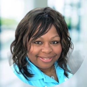 Lynette Smith faces the camera for her professional headshot. She is wearing an aqua polor, silver jewelry, and is smiling. Her brown wavy hair falls past her shoulders.