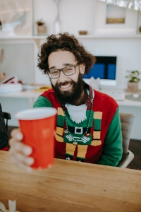 Image of bearded man in colourful Christmas sweater offering a coffee cup